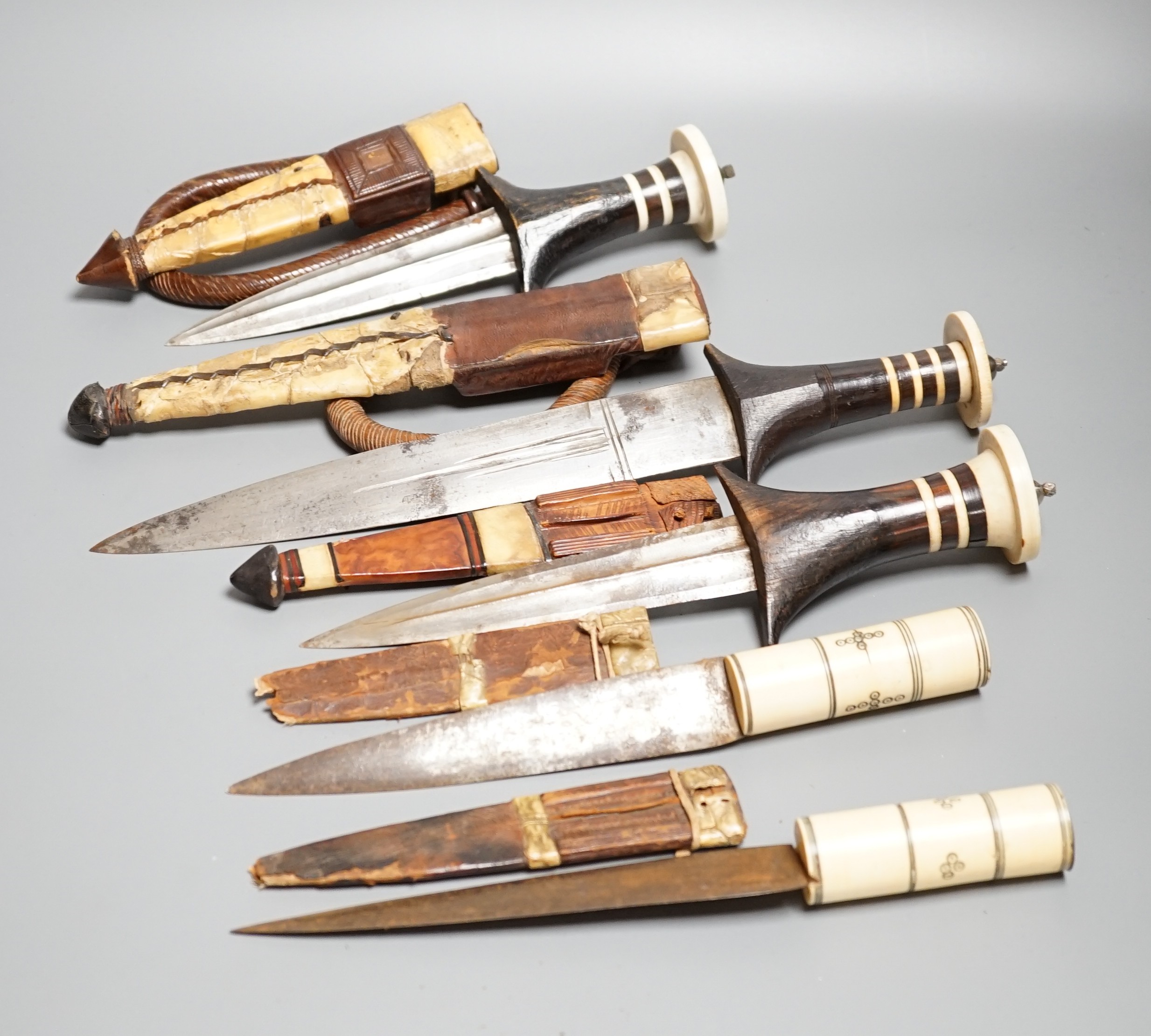 Five assorted African Nilotic tribal daggers c.1900, comprising three with turned ivory mounted ebony handles (two with silver pommels); and two further with cylindrical ivory handles, all in their leather sheaths, maxim